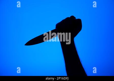 Messerstechergesten-Silhouette schwarz auf blauem Hintergrund, Studioaufnahme unerkennbar. Stockfoto