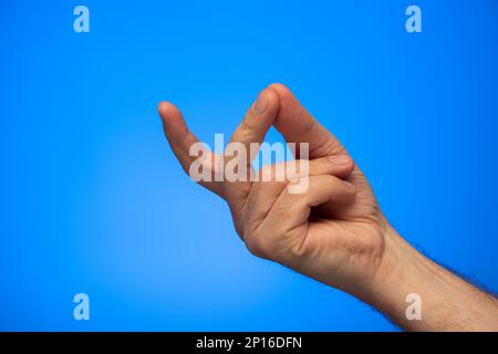 Weiße männliche Hand, die ein Fingerschnipp-Studio auf blauem Hintergrund fotografiert. Stockfoto