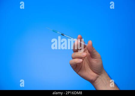 Einweg-Spritze mit Nadel in der Hand gehalten von einem kaukasischen männlichen Handstudio, isoliert auf blauem Hintergrund. Stockfoto