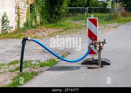 Standrohr mit angeschlossenem blauem Schlauch auf einem Gehweg für Fußgänger. Rote und weiße Kunststoffbarriere. Stockfoto