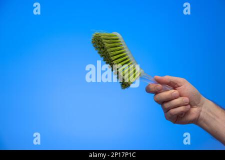 Weiße männliche Hand mit einem grünen Kehrpinsel aus Plastik isoliert auf blauem Hintergrund Studio-Aufnahme. Stockfoto