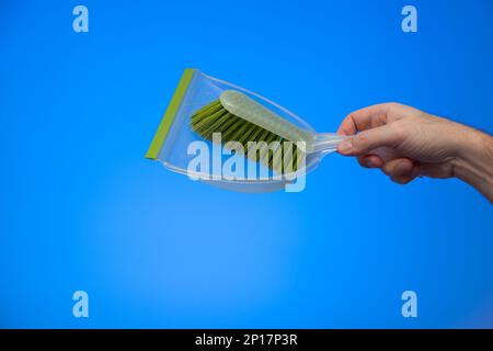 Weiße männliche Hand mit einem grünen Kehrpinsel aus Plastik isoliert auf blauem Hintergrund Studio-Aufnahme. Stockfoto