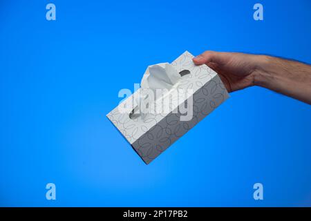 Kaukasische männliche Hand, die eine Schachtel aus Papier Hygienetücher hält, um eine Opfergeste isoliert auf blauem Hintergrund Studioaufnahme zu machen. Stockfoto