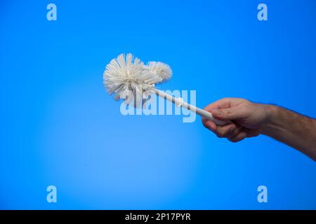 Weiße männliche Hand mit einer weißen Plastik-Toilettenbürste isoliert auf blauem Hintergrund Studioaufnahme. Stockfoto