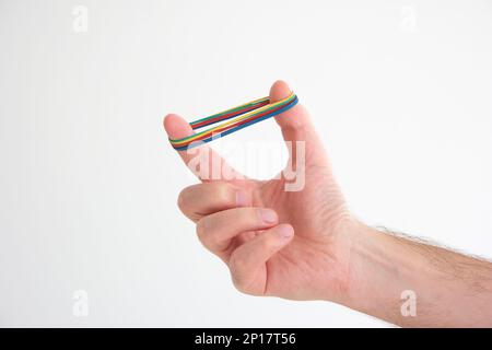 Mehrfarbige Gummibänder, die um die männlichen kaukasischen Handfinger gedehnt sind, isoliert auf weiß. Stockfoto