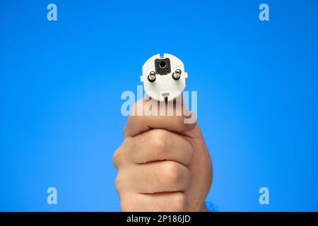 Weißer Gummistecker, der von einem kaukasischen Stecker mit der Hand gehalten wird, isoliert auf blau. Stockfoto