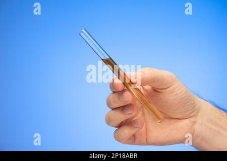 Medizinische Glasröhre mit dunkler Flüssigkeit in der Hand gehalten von kaukasischen männlichen Handstudio Aufnahme isoliert auf blauem Hintergrund. Stockfoto