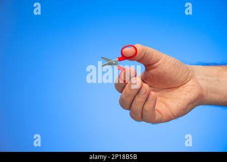 Sehr kleine Schere in der Hand gehalten von einem weißen männlichen Handstudio isoliert auf blauem Hintergrund. Stockfoto