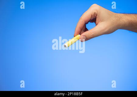 Kleine Rolle gelber Nähgarn, die von einem weißen männlichen Handstudio gehalten wird, isoliert auf blauem Hintergrund. Stockfoto