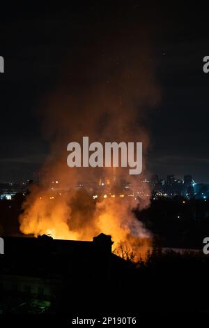 In der Nähe brennendes Gebäude mit orangefarbenen Flammen, Parks und Rauch von einem Feuer in einem Wohnhaus in der Nacht. Stockfoto