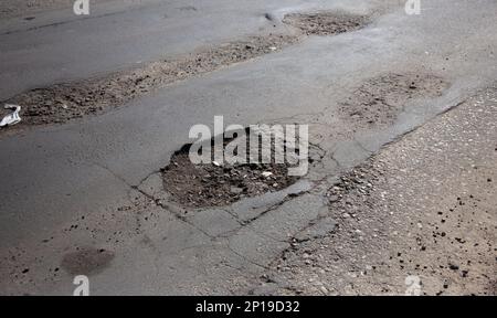 Beschädigte Asphaltstraße mit Schlaglöchern durch Gefrier- und Auftauzyklen im Winter. Stockfoto