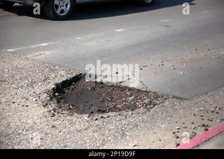 Beschädigte Asphaltstraße mit Schlaglöchern durch Gefrier- und Auftauzyklen im Winter. Stockfoto