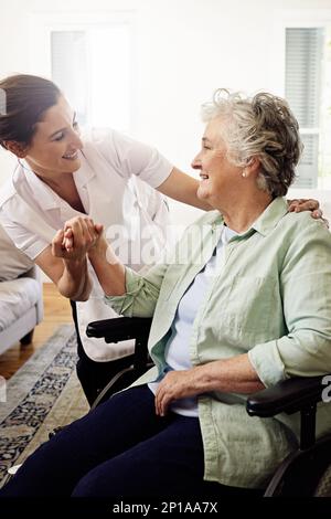 Sie ist so gut mit ihren Patienten. Aufnahme eines lächelnden Betreuers, der einer älteren Frau im Rollstuhl zu Hause hilft. Stockfoto