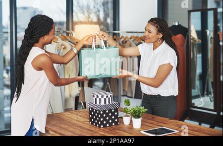 Sie leistet ihren Beitrag für die wirtschaftliche Gesundheit. Eine kleine Aufnahme eines jungen Ladenbesitzers, der einem Kunden ein Paket über den Ladentisch übergab. Stockfoto