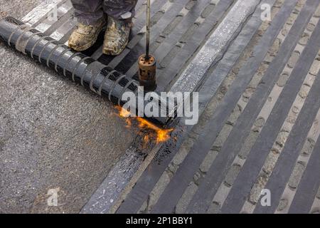 Arbeiter, die mit einem Propangasbrenner zum Schweißen von Bitumen-Platten eine Dampfsperre auf dem Dach anbringen. Stockfoto