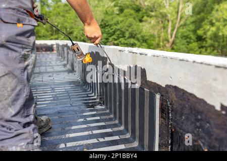 Arbeiter, die mit einem Propangasbrenner zum Schweißen von Bitumen-Platten eine Dampfsperre auf dem Dach anbringen. Stockfoto