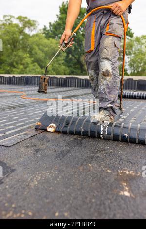 Arbeiter, die mit einem Propangasbrenner zum Schweißen von Bitumen-Platten eine Dampfsperre auf dem Dach anbringen. Stockfoto