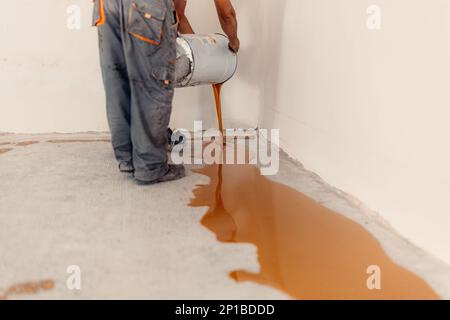 Ein Arbeiter, der einen gelben Epoxidharzbehälter auf dem Boden aufträgt. Stockfoto