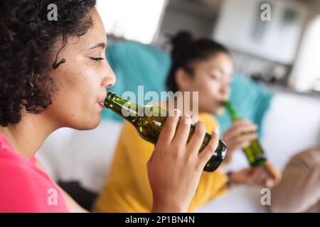 Fröhliche, vielfältige Freunde, die auf dem Boden sitzen und Bier trinken Stockfoto