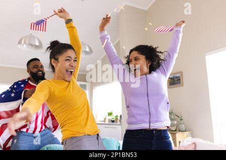 Fröhliche, vielfältige Freunde sitzen auf dem Sofa, sehen sich ein Fußballspiel an und feiern Stockfoto