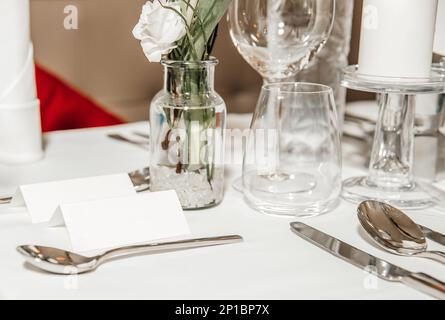 Besteck auf einem festlichen Tisch in einem Restaurant, ein Namensschild, eine Blumenvase, eine weiße Kerze, Weingläser und Gläser für Wasser und Wein Stockfoto