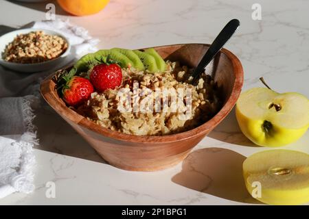 Gesunde hausgemachte Haferflocken in einer Holzschüssel mit Früchten auf einem weißen Tisch Stockfoto