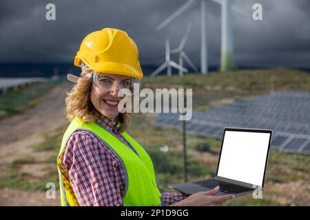 Weibliche Ingenieurin benutzt ihren Laptop, während sie im Solarkraftwerk arbeitet, und prüft mit einem Modell. Stockfoto