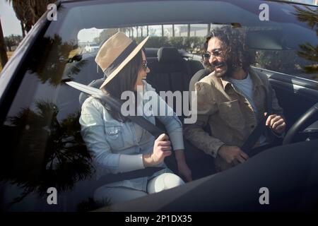 Ein junges weißes glückliches Paar, das sich in einem Cabrio anschnallt. Sicherheitsgurt, sicheres Fahren. Stockfoto