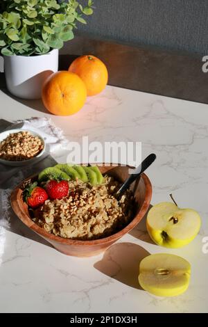 Gesunde hausgemachte Haferflocken in einer Holzschüssel mit Früchten auf einem weißen Tisch Stockfoto