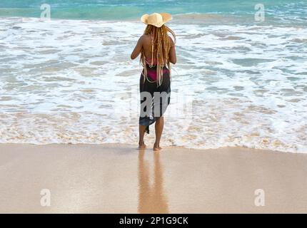 Oahu, Hawaii, USA, - 12. Februar 2023: Eine afroamerikanische Frau, die am Ufer im Sand am Nordufer der hawaiianischen Insel O steht Stockfoto