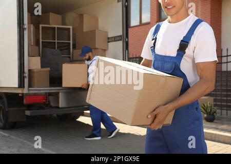 Arbeiter, die Kisten aus dem Lieferwagen im Freien entladen. Umzugsdienst Stockfoto