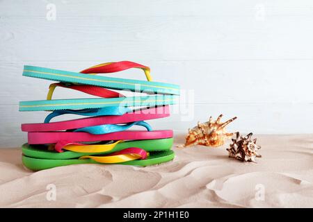 Viele verschiedene Flip Flops und Muscheln auf Sand vor weißem Hintergrund Stockfoto