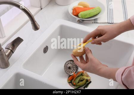 Eine Frau schälte Kartoffeln über der Küchenspüle mit Müllschlucker zu Hause, Schließung Stockfoto