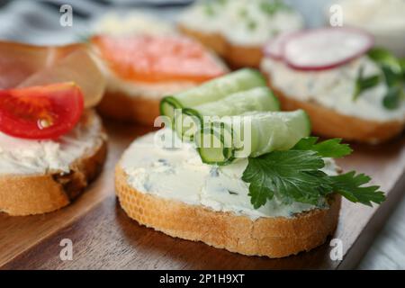 Getoastetes Brot mit Frischkäse, Gurke und Petersilie auf Holzbrett, Nahaufnahme Stockfoto