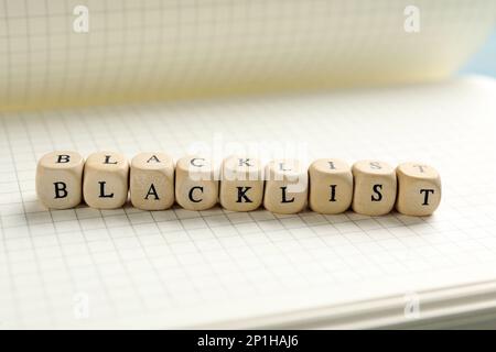 Holzwürfel mit dem Wort Blacklist auf Notizbuch, Nahaufnahme Stockfoto