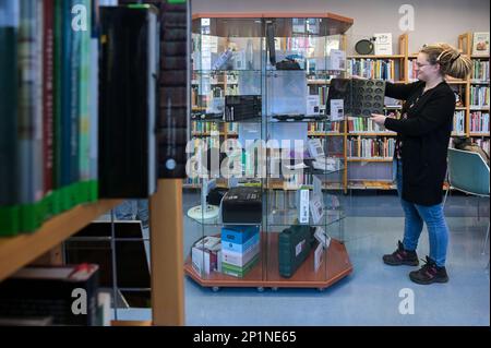 02. März 2023, Sachsen-Anhalt, Halle (Saale): Bibliotheksangestellte Sara Schumann stellt eine Brezel-Backpfanne in den Schaukasten der 'Bibliothek der Dinge'. In der Stadtbibliothek Halle (Saale) können neben viel Literatur auch Gegenstände in einer „Bibliothek der Dinge“ ausgeliehen werden. Das sind Dinge, die nicht immer benutzt werden. Um Kosten zu sparen und die Umwelt zu schützen, müssen diese Artikel nicht von jedem gekauft werden, sondern können für einen Zeitraum von vier Wochen ausgeliehen werden. Foto: Heiko Rebsch/dpa Stockfoto