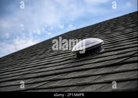 Kuppelförmiges Sonnenröhren-Oberlicht auf Asphalt-Schindeldach Stockfoto