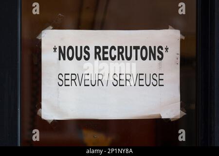 Papier, das im Fenster eines Restaurants mit französischer Aufschrift "Nous Recrutons: Serveur / Serveuse", was auf Englisch bedeutet "Wir stellen ein Stockfoto