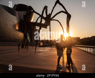 Bilbao, Spanien - 02. August 2022: Ein paar Touristen machen ein Selfie bei Sonnenuntergang neben der Spinne, der Skulptur von Louise Bourgeois mit dem Titel Mamam in Th Stockfoto