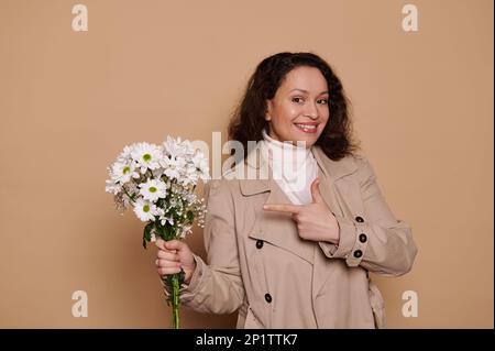 Eine charmante Frau mittleren Alters zeigt auf einen wunderschönen Blumenstrauß. Ein glückliches Geschenk für jeden festlichen Anlass. Frauentag Stockfoto