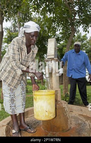 Frau, die Eimer mit klarem Wasser am Brunnen einer Handpumpe im Dorf Kenia füllt Stockfoto