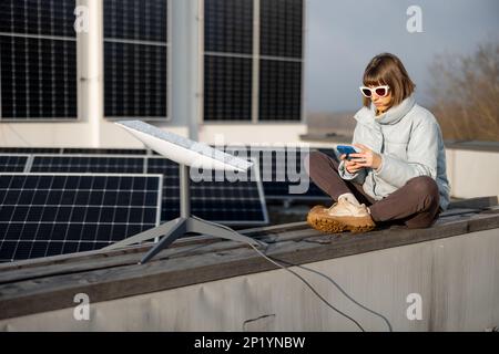 Frau benutzt Starlink Internet auf dem Dach mit Solarpaneelen Stockfoto