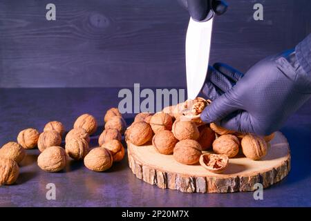 Der Koch schält Walnüsse mit einem Messer in der Küche am Tisch. Stockfoto