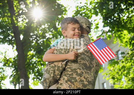 Ein Soldat und sein kleiner Sohn mit der Flagge der USA, die sich im Freien umarmt Stockfoto