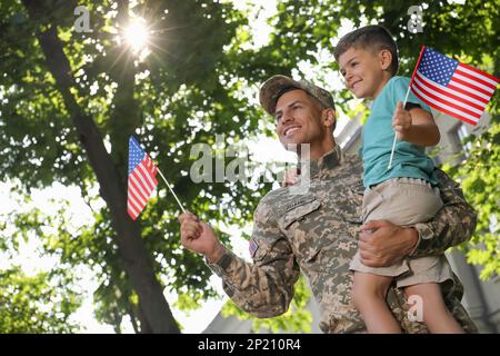 Soldat und sein kleiner Sohn mit amerikanischen Flaggen draußen, Blick aus dem niedrigen Winkel. Veteranentag in den USA Stockfoto