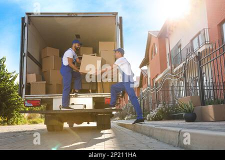 Arbeiter, die Kisten aus dem Lieferwagen im Freien entladen. Umzugsdienst Stockfoto