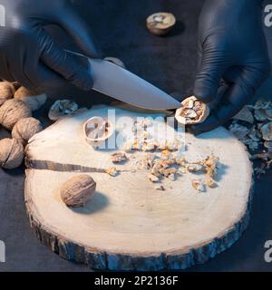 Der Koch schält Walnüsse mit einem Messer in der Küche am Tisch. Stockfoto