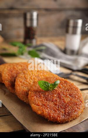 Köstliche gebratene panierte Schnitzel mit Basilikum auf einem Holztisch Stockfoto