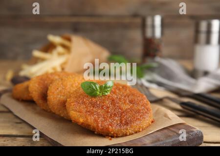 Köstliche gebratene panierte Schnitzel mit Basilikum auf einem Holztisch, Nahaufnahme Stockfoto