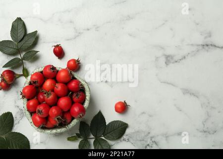 Reife Rosenbeeren mit grünen Blättern auf einem weißen Marmortisch, flach liegend. Platz für Text Stockfoto